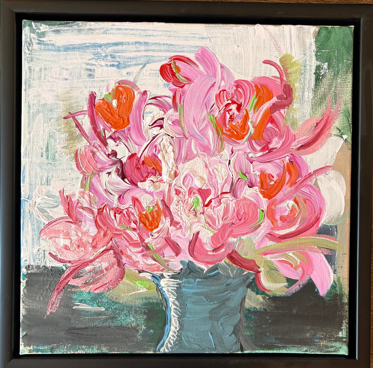 Framed abstract painting with pink and orange flowers on a wooden surface