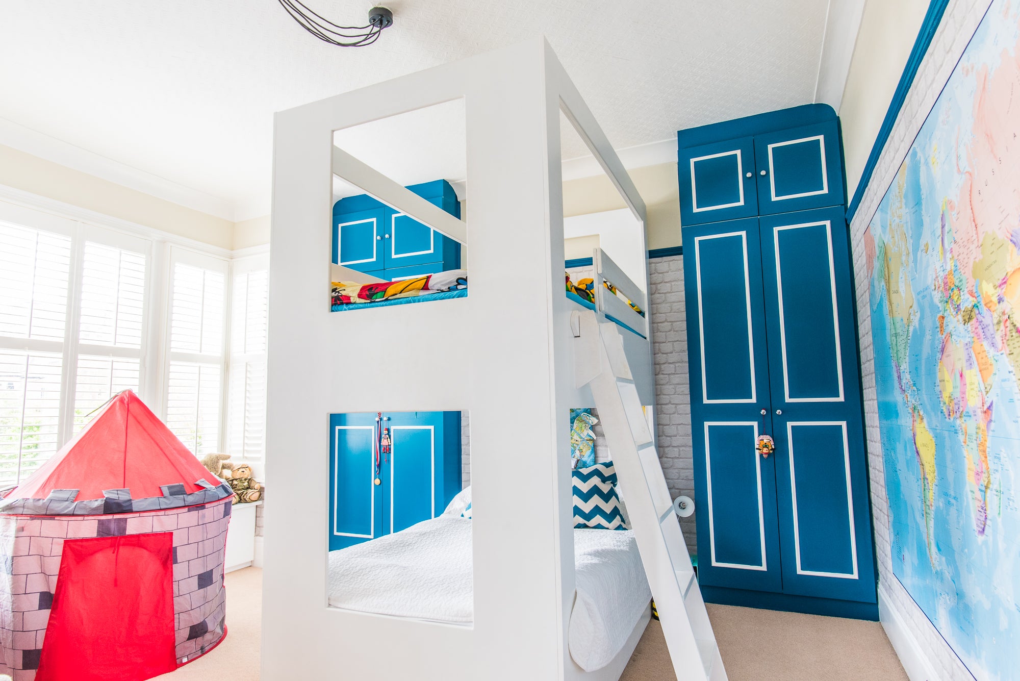 Children's bedroom with bunk beds, a red play tent, and world map on the wall.