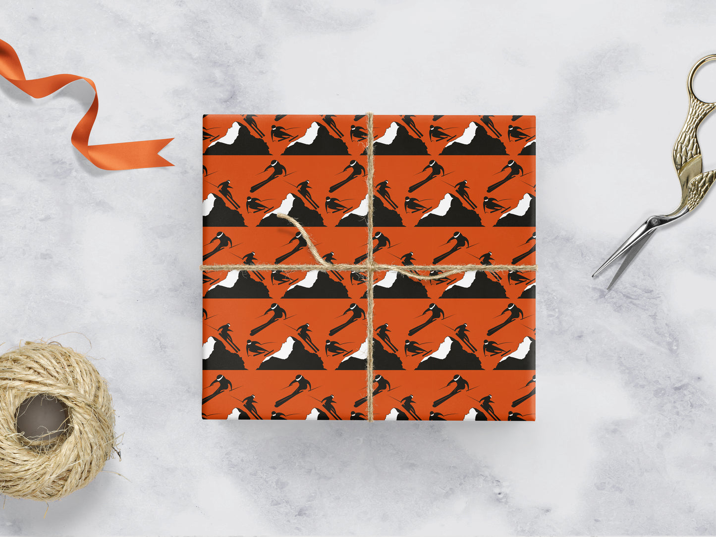 orange gift wrapping with rows of 3 skiers on either side of a mountain